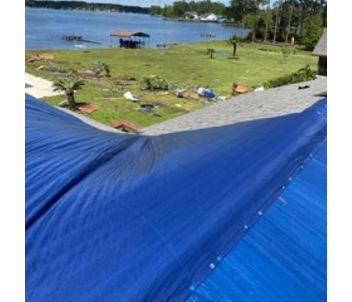 A damaged roof is shown covered by a blue tarp